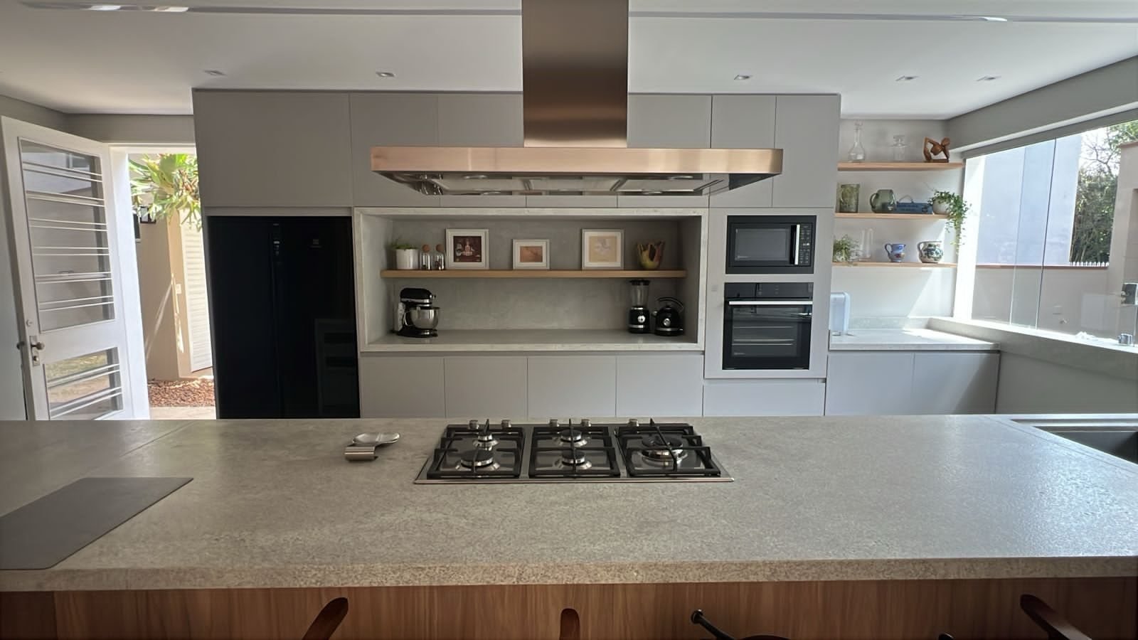 Ilha de cozinha em granito com cooktop embutido, nicho em pedra e coifa