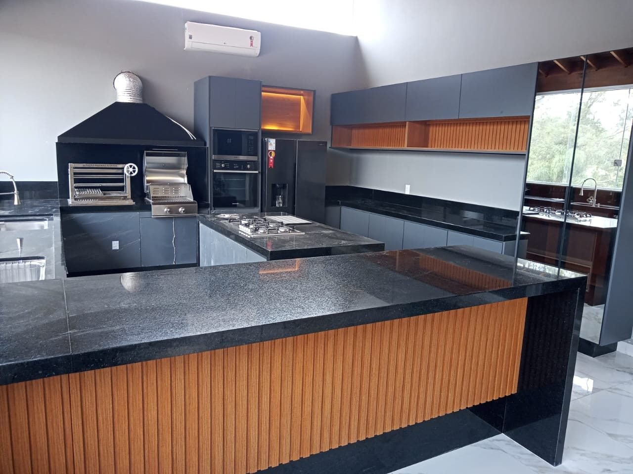 Área gourmet com churrasqueira, ilha com cooktop e bancadas em granito preto polido