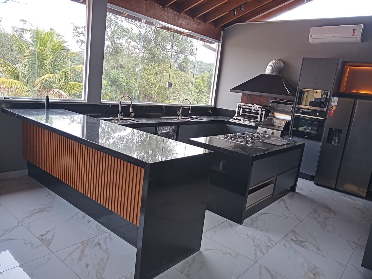 Área gourmet com bancada em U em granito preto, frente em ripado de madeira e duas cubas