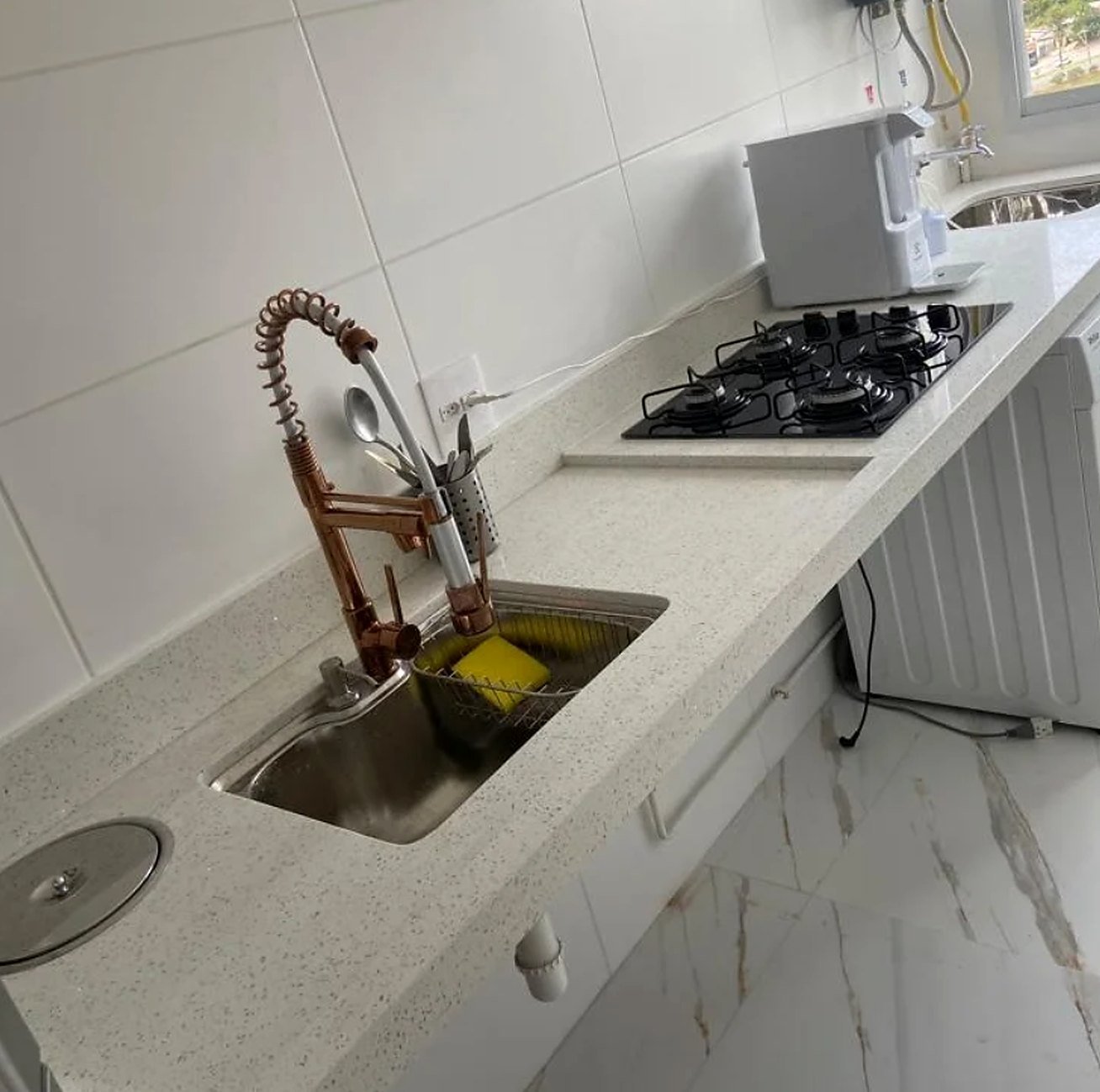 Bancada de cozinha em pedra branca com cuba de inox, torneira em cobre e cooktop