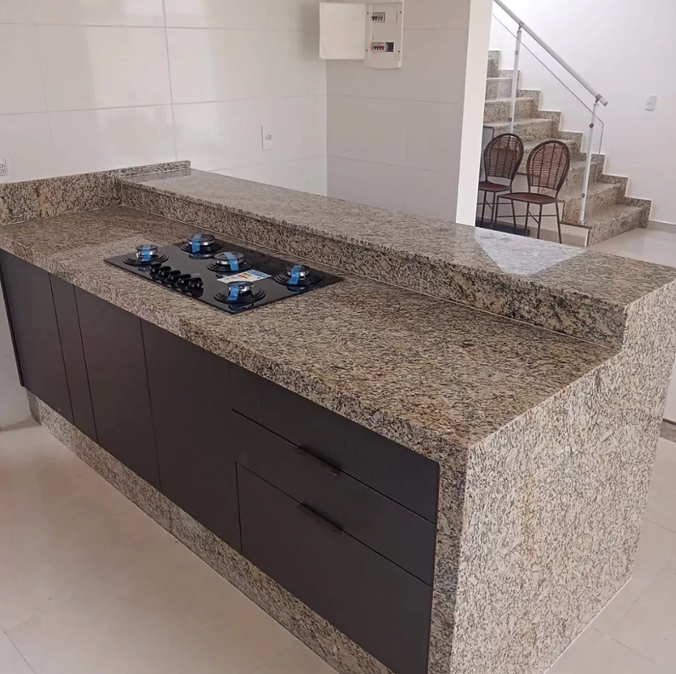 Bancada de cozinha em granito com cooktop, balcão elevado e laterais revestidas em pedra