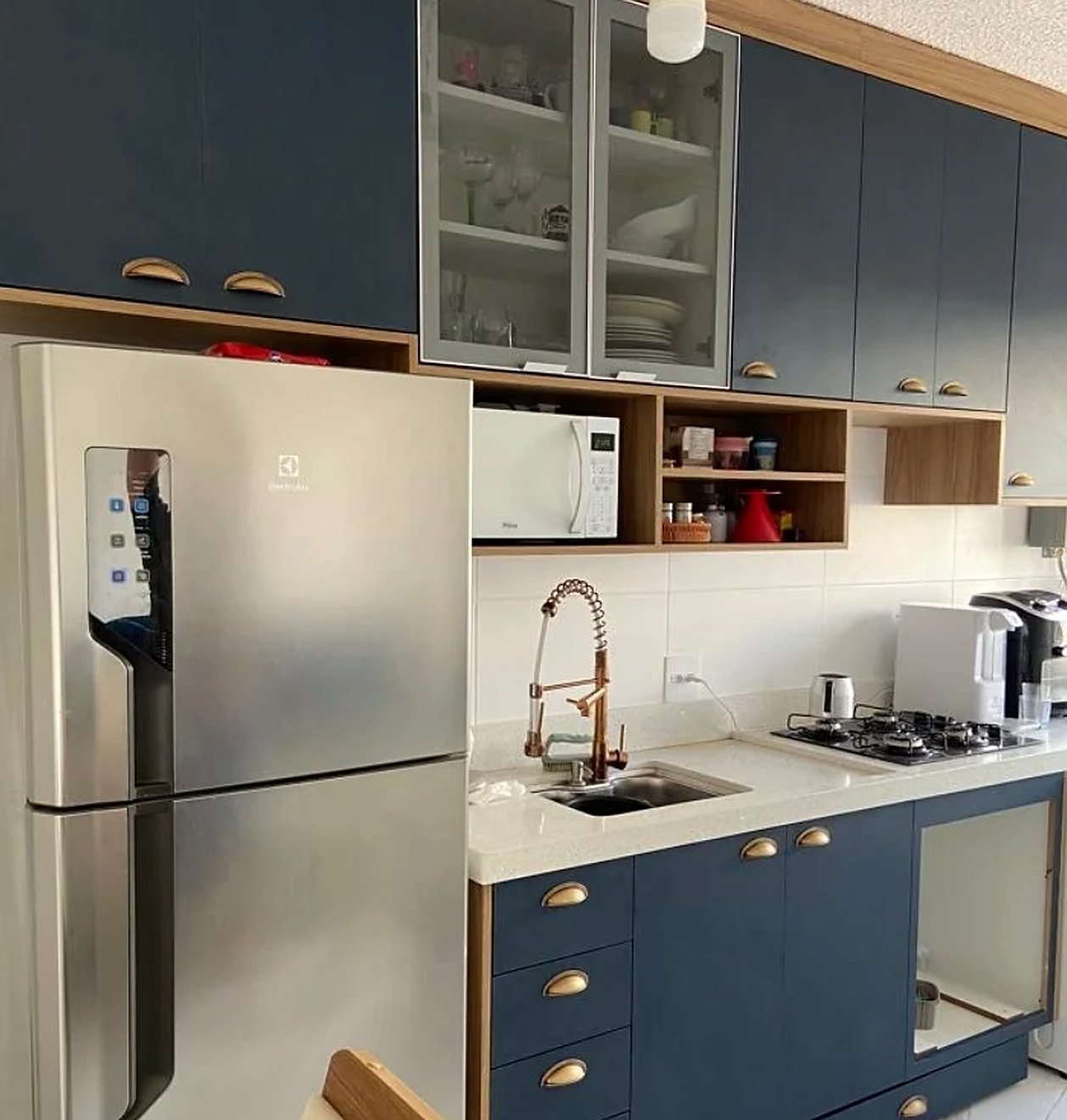 Cozinha com bancada branca, cuba e cooktop, armários azuis e torneira em cobre