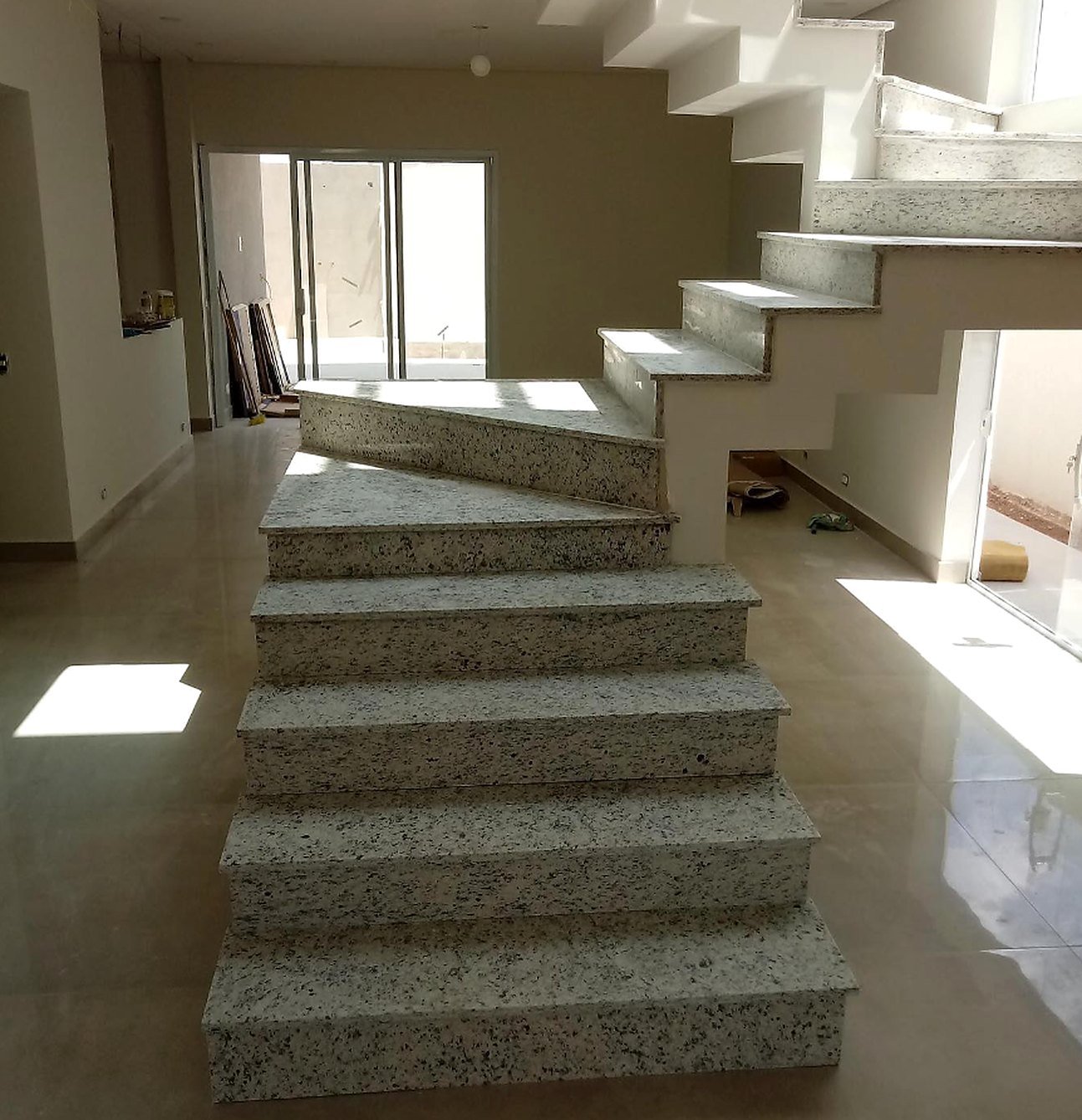 Escada em granito claro, com degraus em curva, instalada em sala ampla