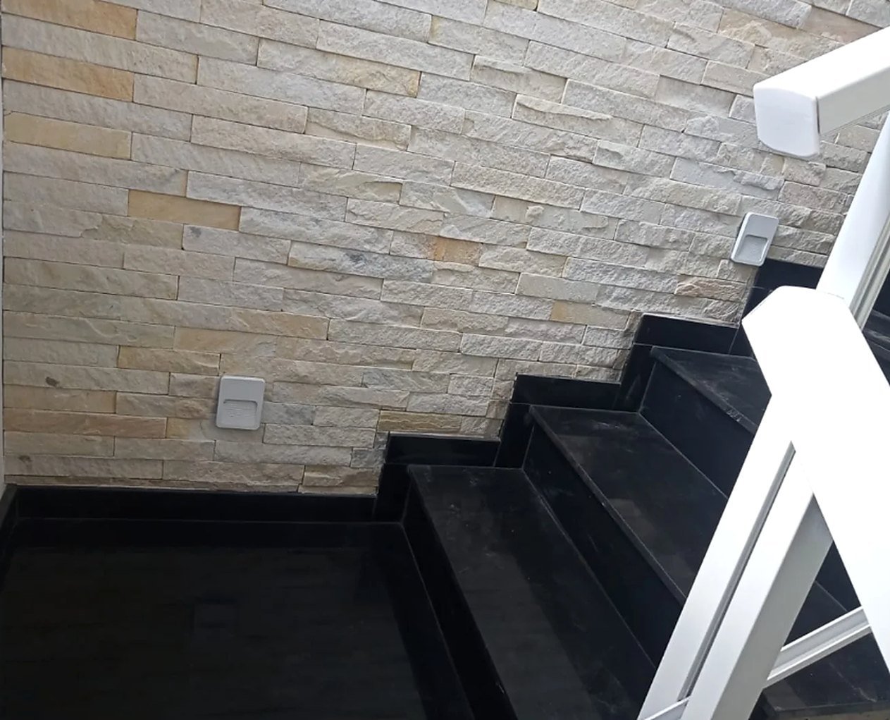 Escada em granito preto ao lado de parede revestida em pedra
