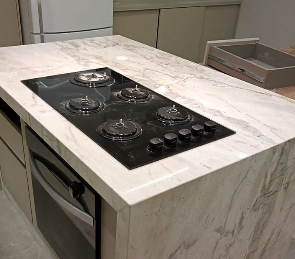 Ilha de cozinha em granito branco com cooktop embutido e lateral em cascata