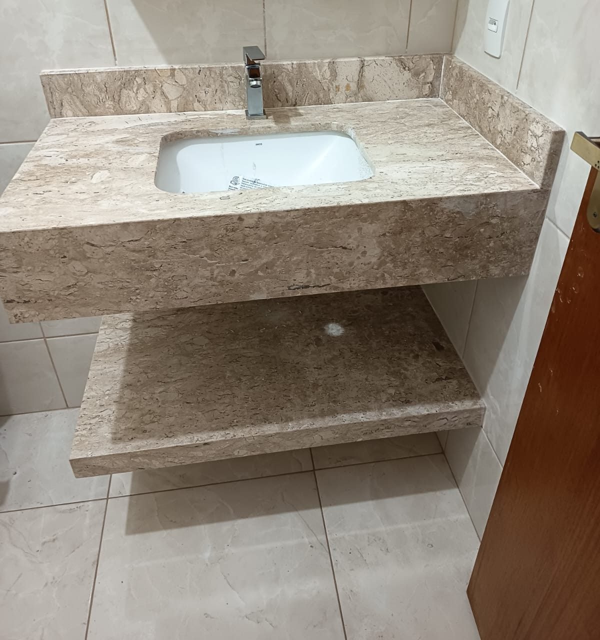 Lavatório suspenso em mármore travertino com cuba embutida e prateleira inferior na mesma pedra